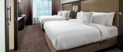 A hotel room with two beds, a TV, and a large window with curtains.