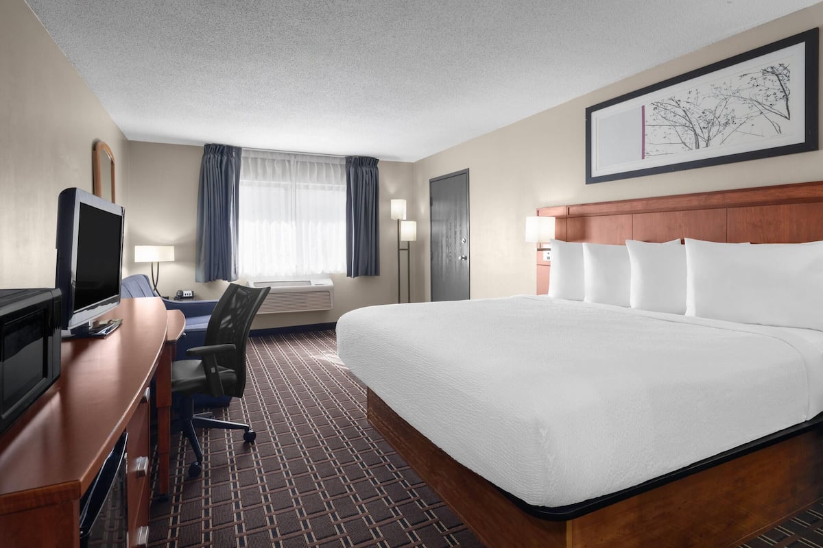 A hotel room with a large bed, a desk with a computer, a television, and a window with curtains.
