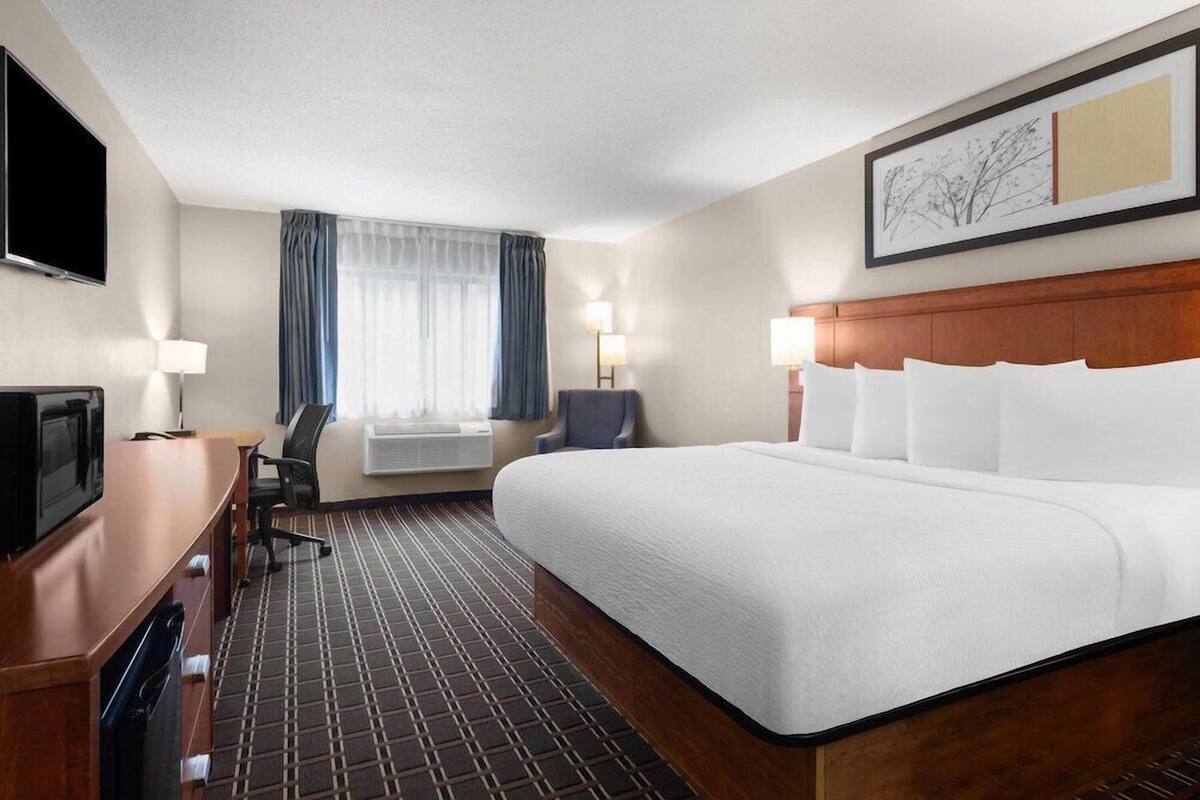 A hotel room with a bed, desk, TV, and a window with curtains.