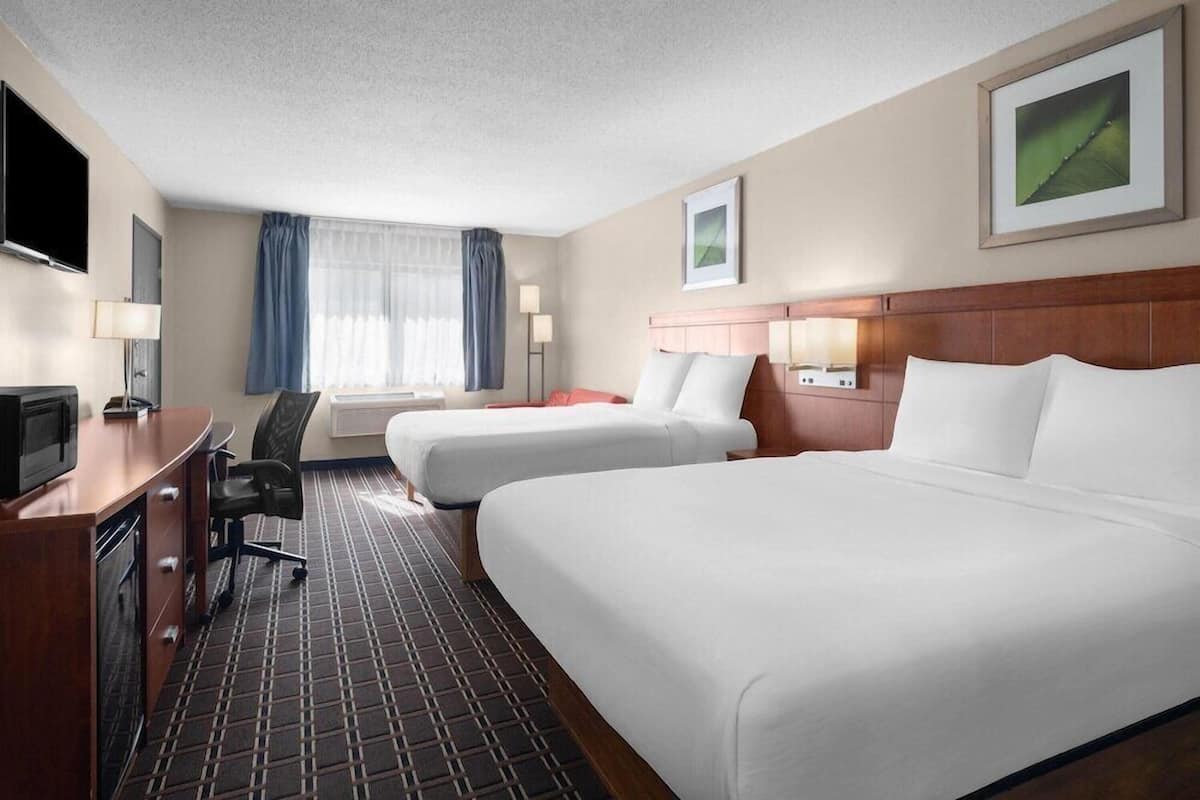 A hotel room with two beds, a desk with a TV, a chair, and a window with curtains.