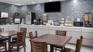 A modern kitchen with a brick backsplash, a flat-screen TV, and various appliances including a coffee maker, microwave, and toaster. - Travelodge by Wyndham Fargo West Acres (Fargo)