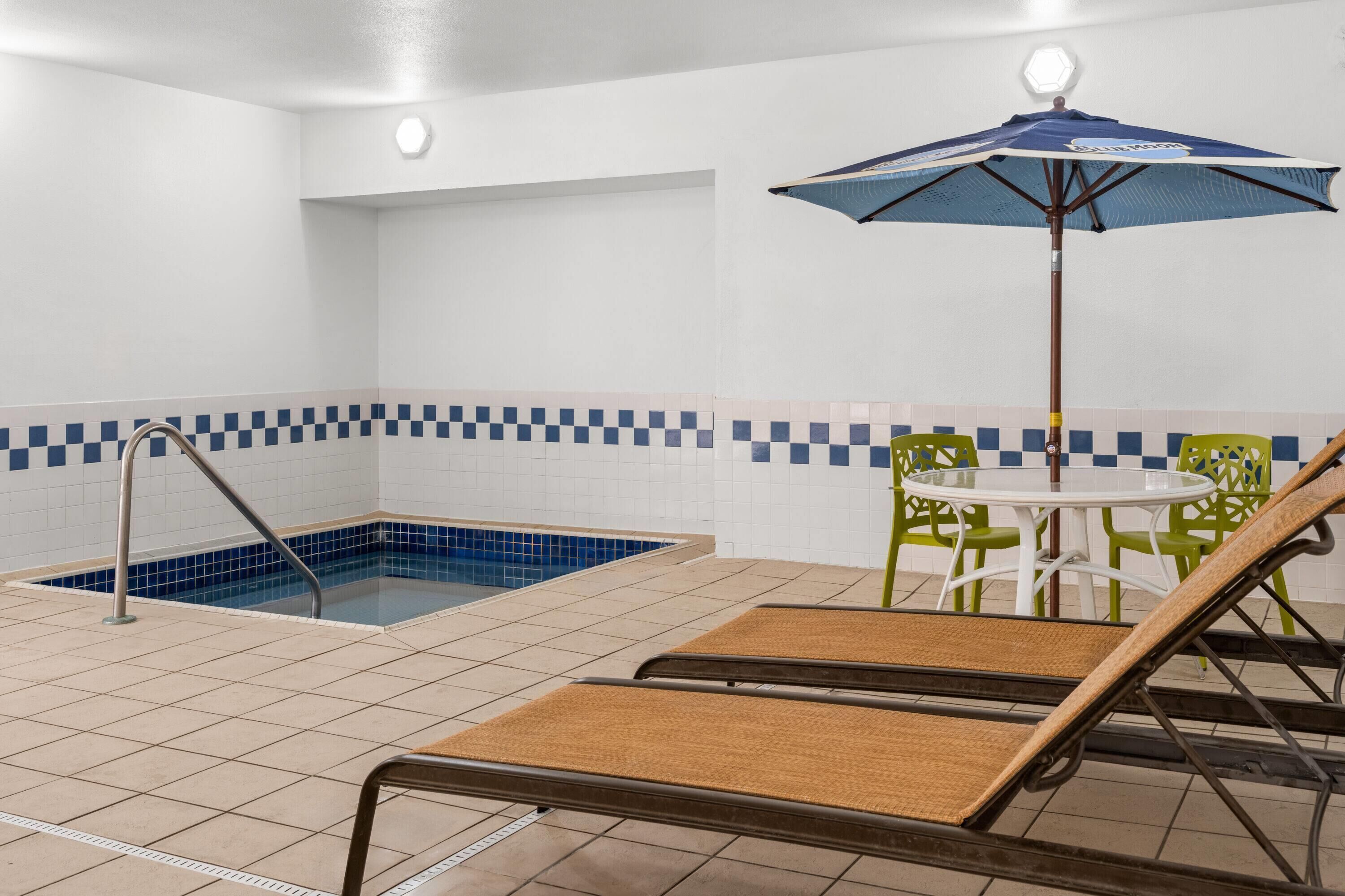 Ein Poolbereich mit einer blauen und weißen Kachelwand, einer Liege, einem Tisch mit Stühlen und einem blauen Sonnenschirm.