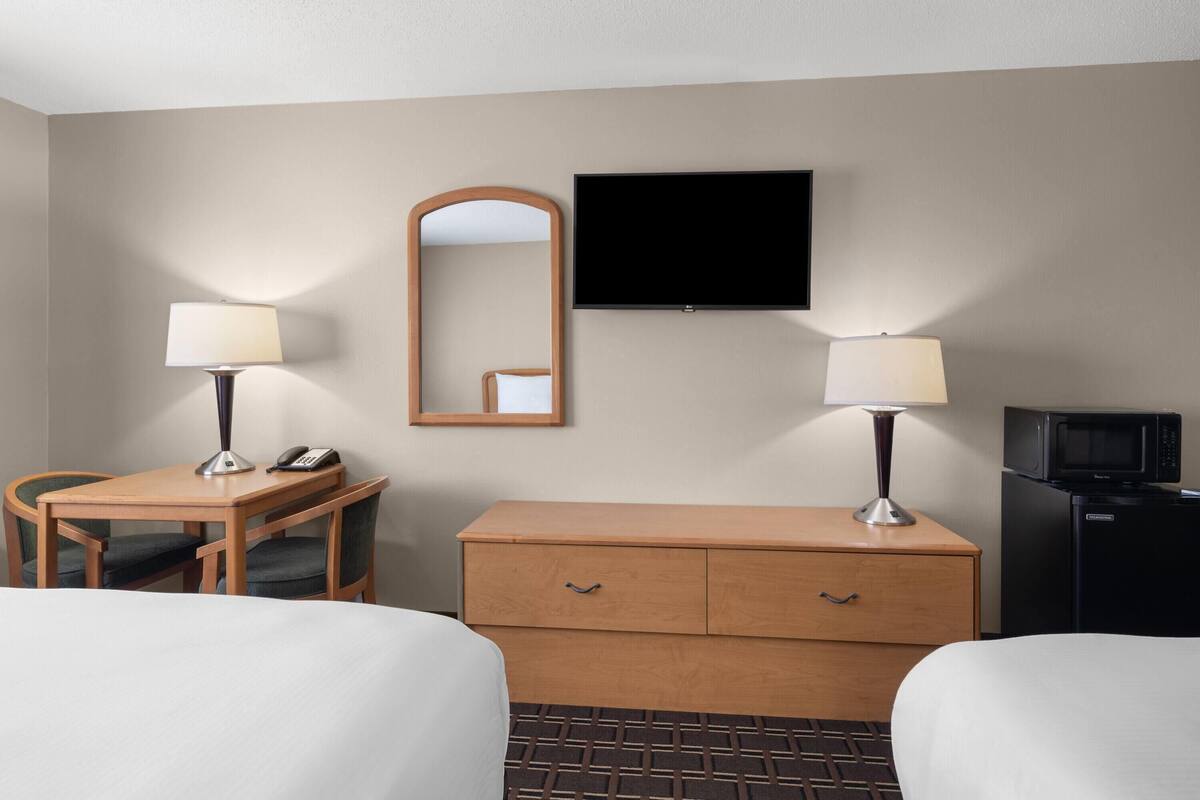 A hotel room with two beds, a desk with a lamp, a dresser, a TV, and a microwave.