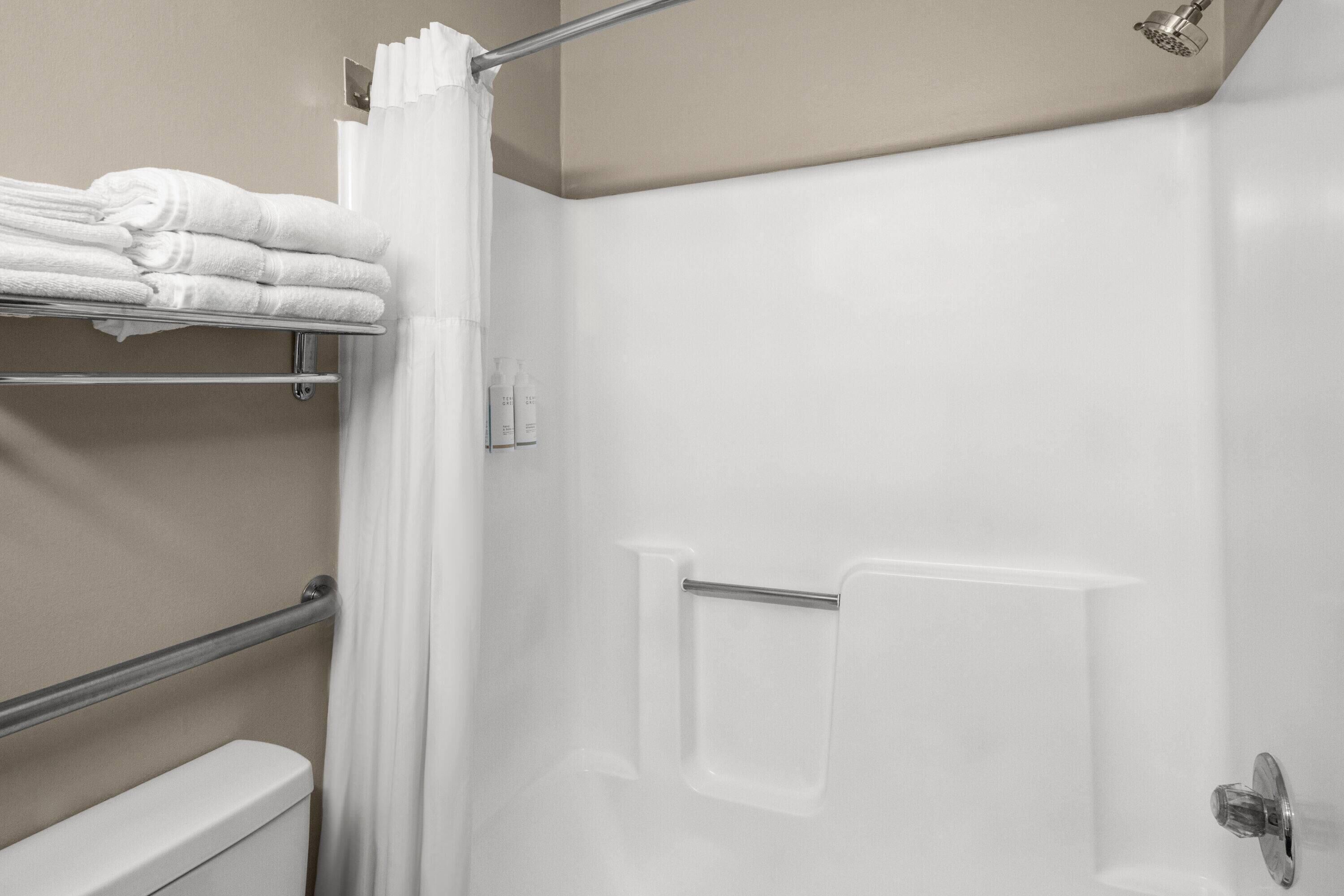 A bathroom with a shower, a toilet, and a towel rack with folded towels.