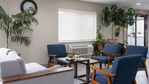 A modern living room with a sofa, blue armchairs, a coffee table, and a clock on the wall. - Travelodge by Wyndham Fargo West Acres (Fargo)