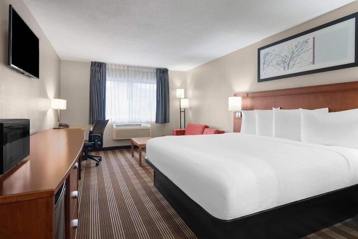 A hotel room with a large bed, a desk, a chair, a flat-screen TV, a window with curtains, and a painting on the wall.