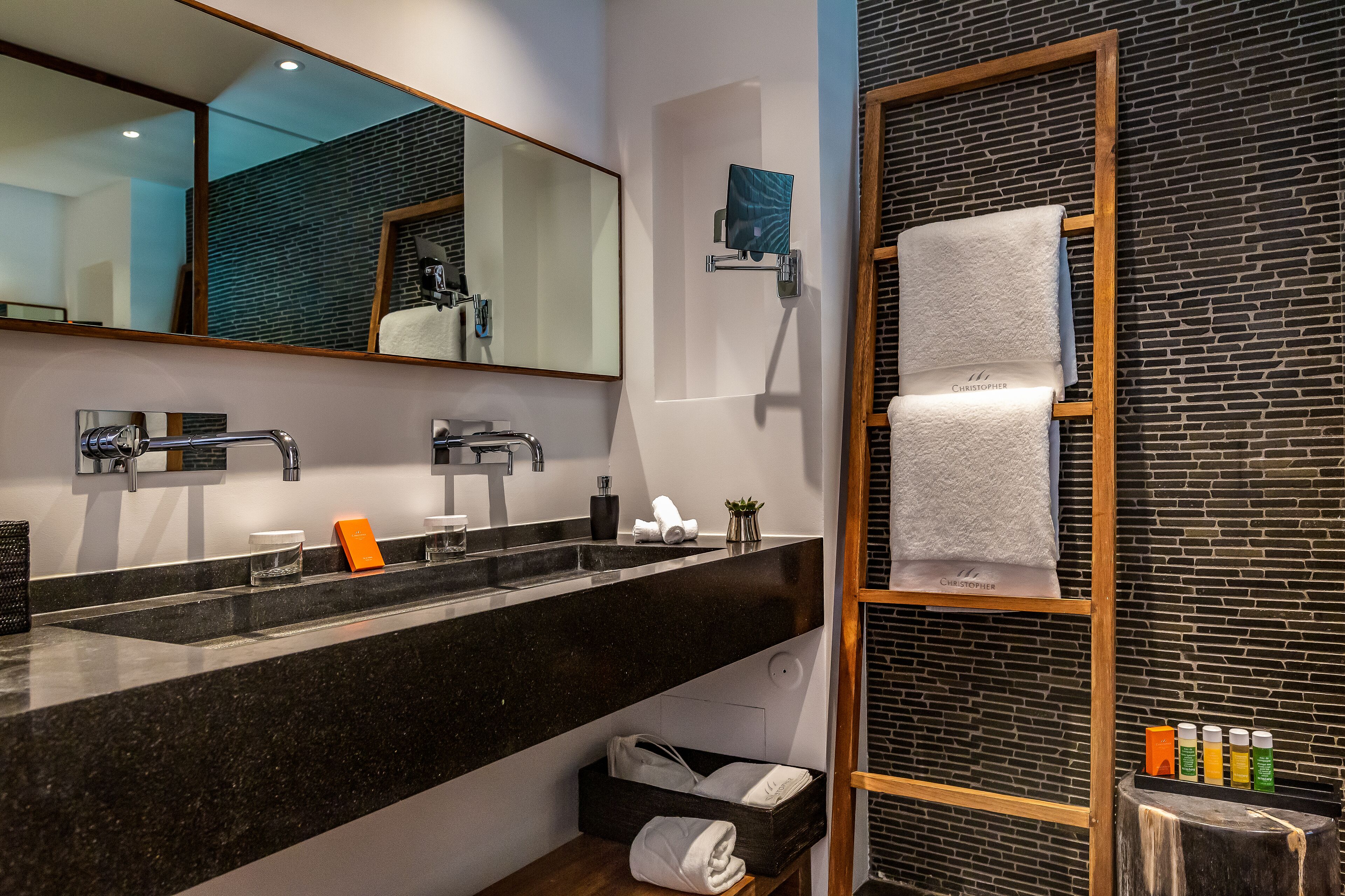 Un baño moderno con encimera negra, un espejo grande, un perchero y una pared con diseño de ladrillo.