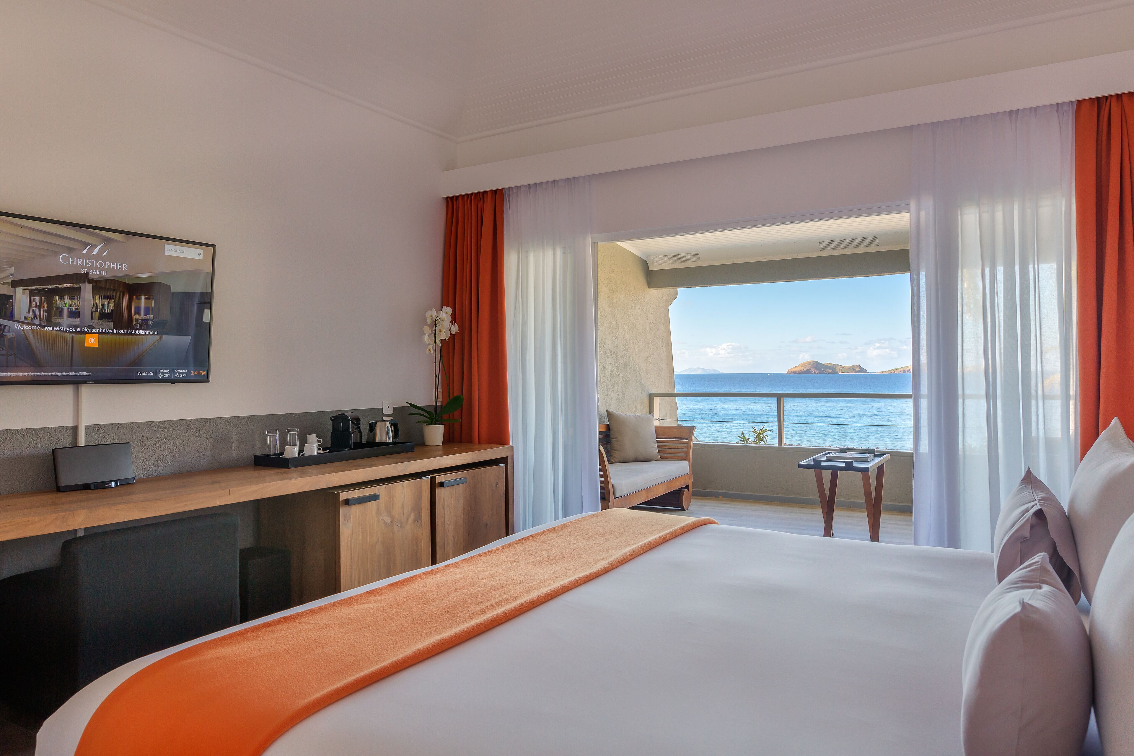 Camera d'albergo con un letto, una scrivania con un computer, un tavolino e vista sul mare.