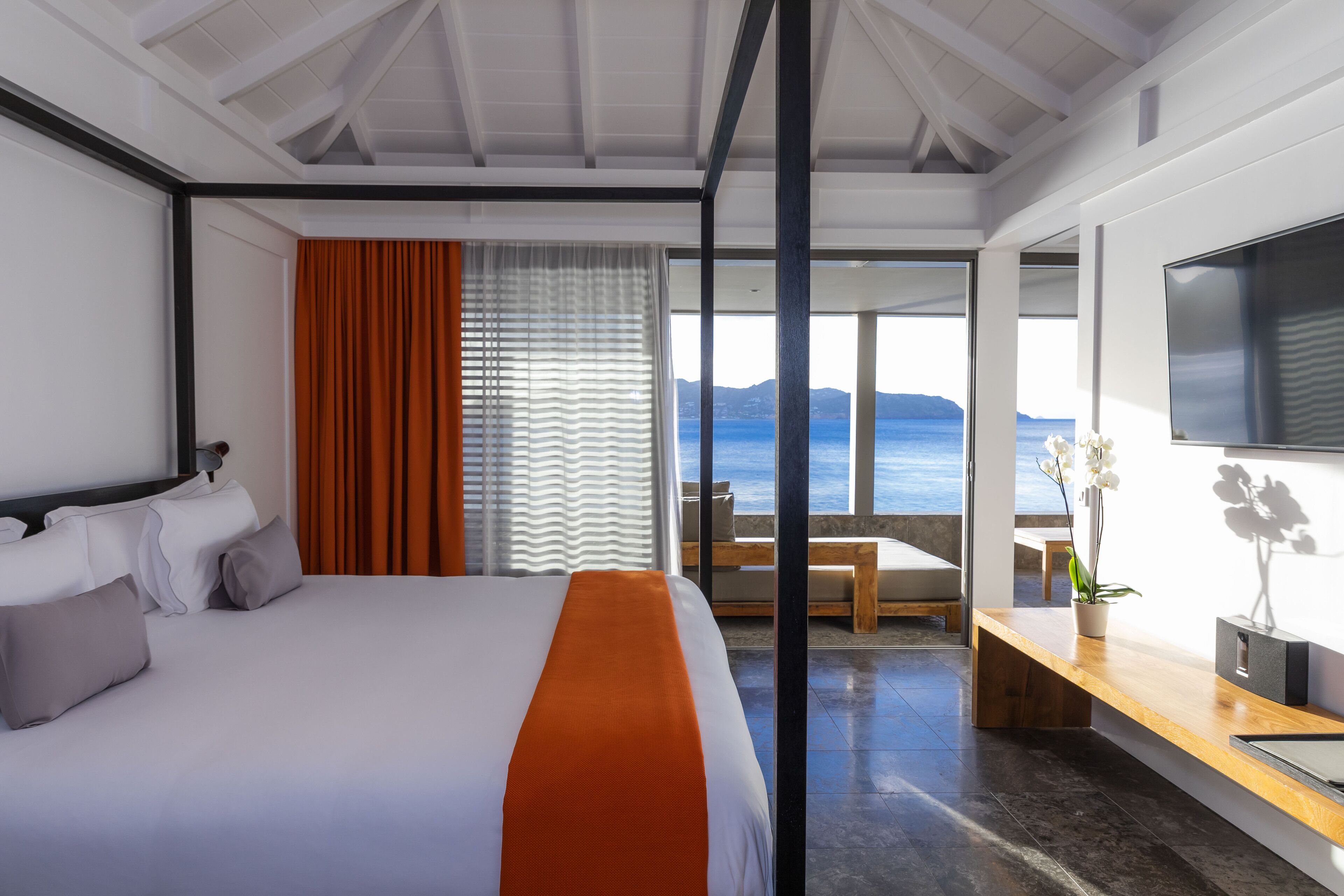A modern hotel room with a large bed, a TV, and a view of the sea.