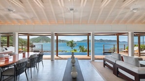 A spacious room with a large dining table and chairs, a sofa, and a decorative vase. The room features large windows with a view of the ocean and hills. - Christopher Hotel (St. Barthelemy)