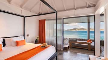 A modern hotel room with a large bed, a balcony with a view of the sea, and a seating area with a table.