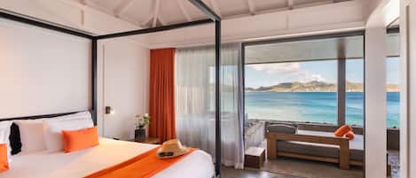 Una habitación de hotel moderna con una cama grande, un balcón con vistas al mar y una zona de estar con una mesa.