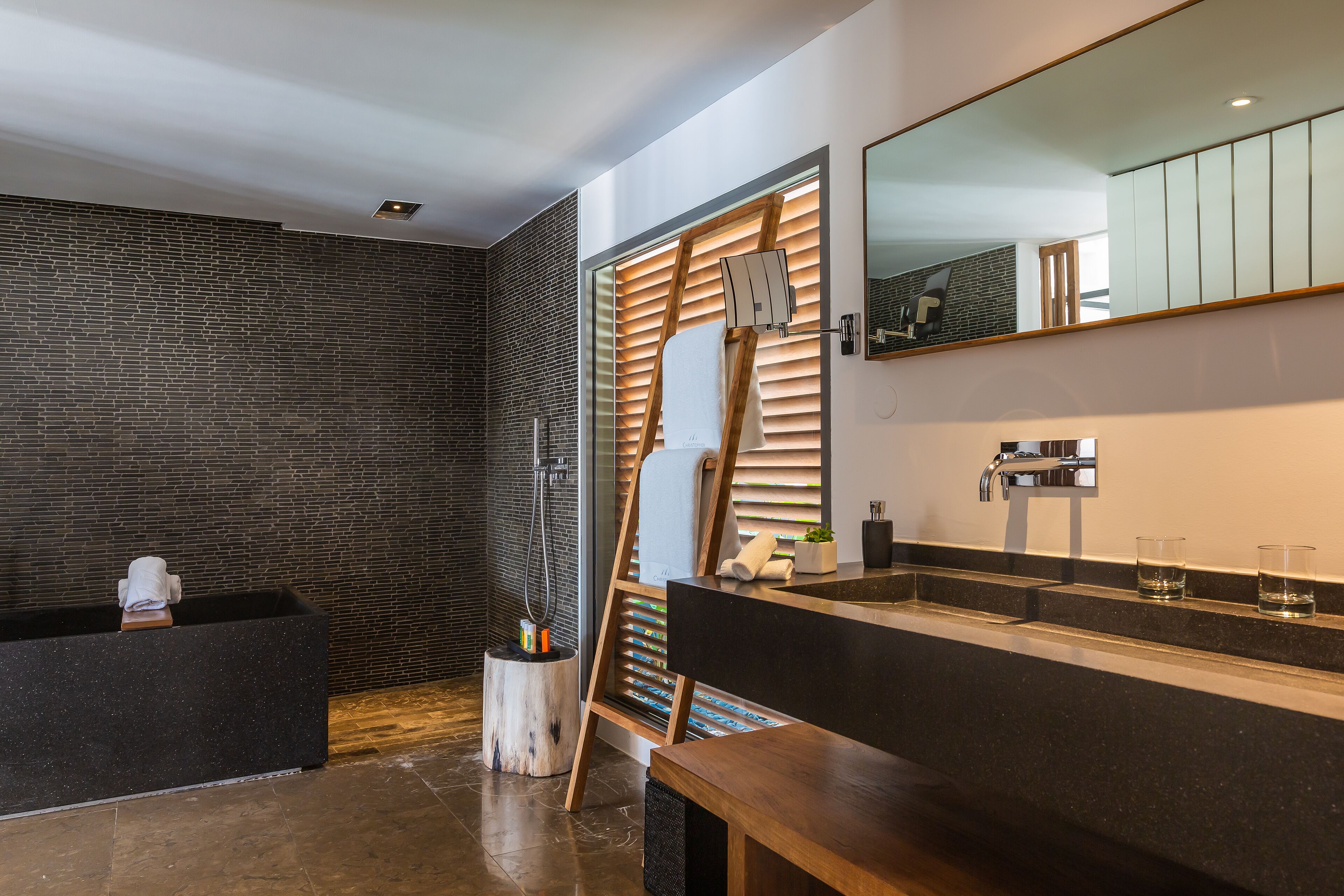 A modern bathroom with a black sink, wooden bench, and a large mirror.