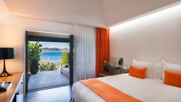 Habitación de hotel moderna con una cama grande, ropa de cama naranja, una mesita de noche, una lámpara y vista al mar a través de un ventanal.