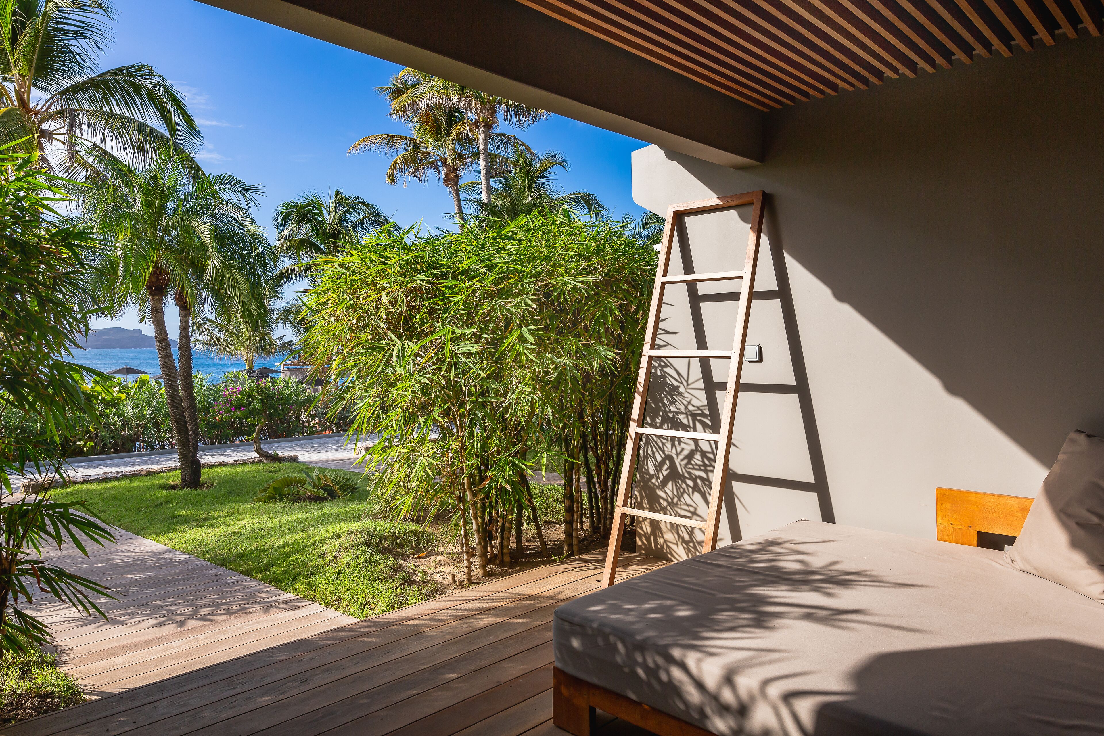 Une chambre avec un lit en bois, une échelle et une vue sur des palmiers et une plage.