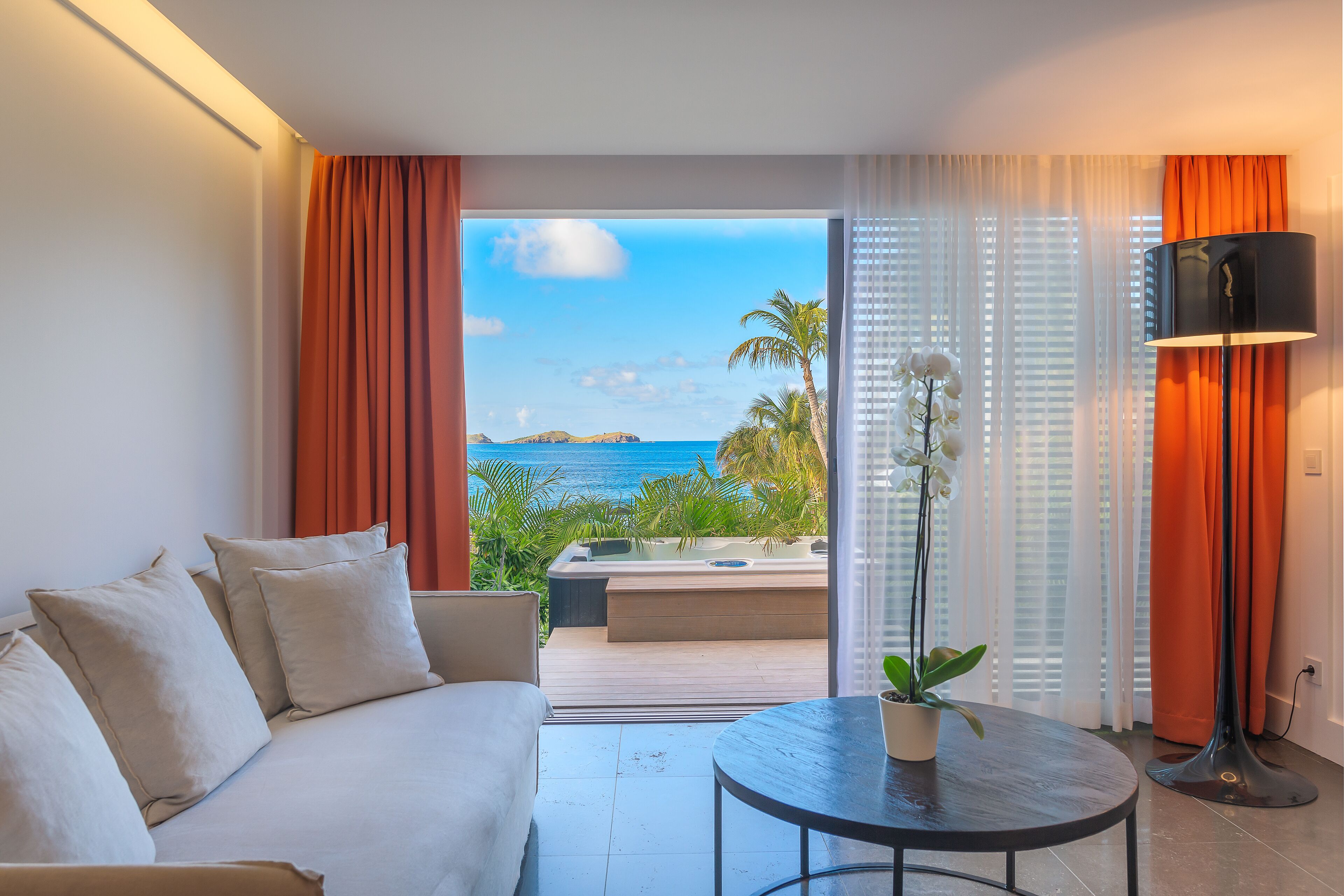 Una habitación de hotel moderna con balcón, un sofá, una mesa y vista al océano.