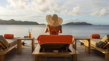 A wooden deck with lounge chairs and a table, overlooking a calm sea and distant hills.
