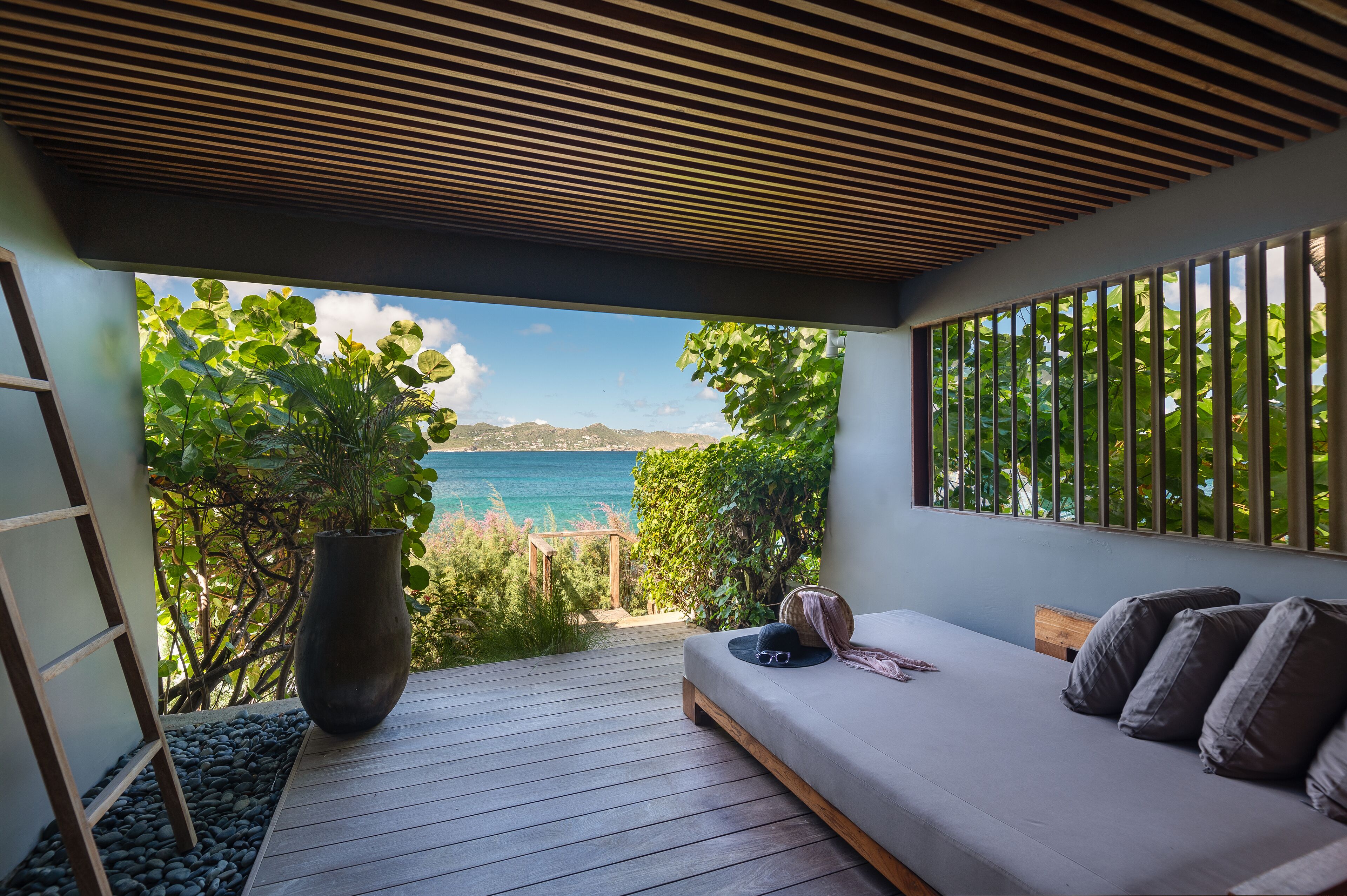Un dormitorio con vista al mar, una planta grande en maceta y una terraza de madera.