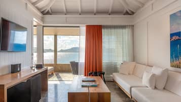 Una sala de estar moderna con una mesa de centro de madera, un sofá blanco, un televisor de pantalla plana y un amplio ventanal con vista al mar.