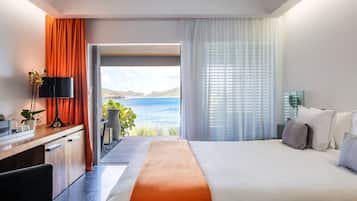 A modern hotel room with a large bed, a desk, and a view of the sea.