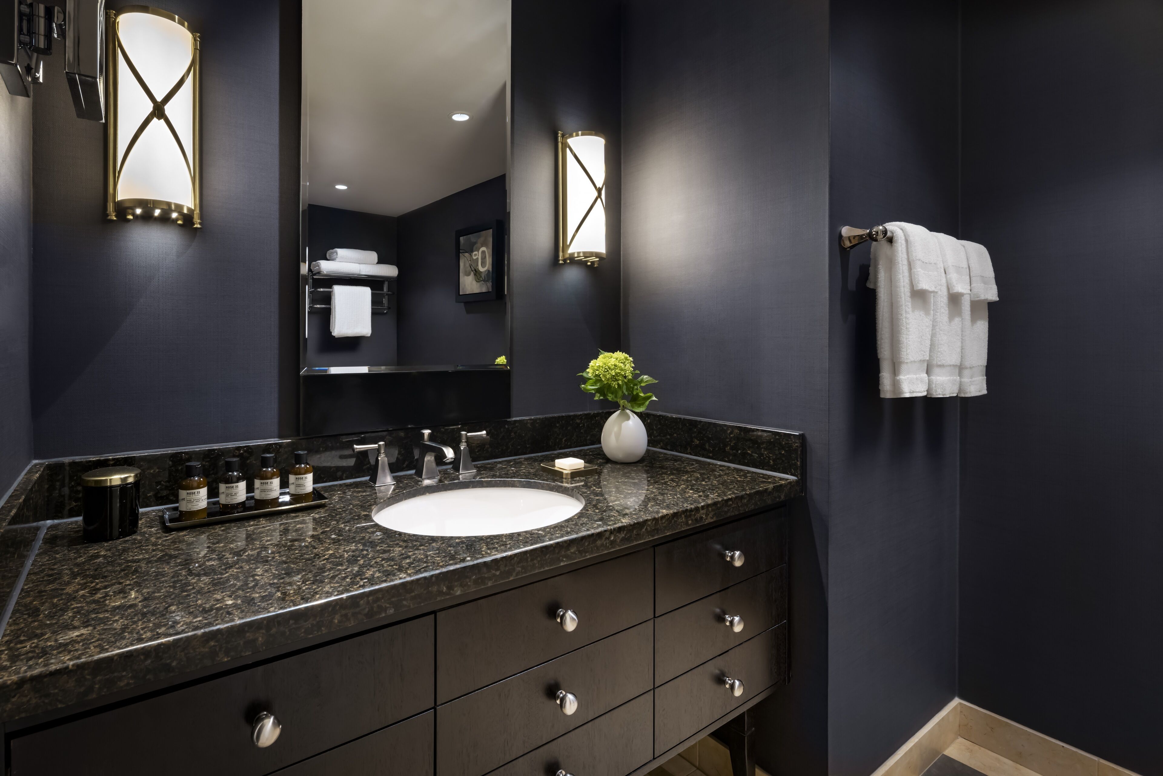 Un baño moderno con una pared oscura, encimera de granito, lavabo blanco y un espejo.