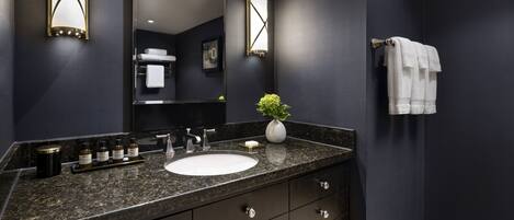 Un baño moderno con una pared oscura, encimera de granito, lavabo blanco y un espejo.