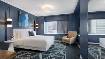 A modern hotel room with a large bed, a small table, a chair, and a large window with curtains.