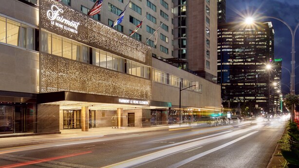 A hotel with a modern facade, multiple flags, and a well-lit entrance. - Fairmont The Queen Elizabeth (Montreal)