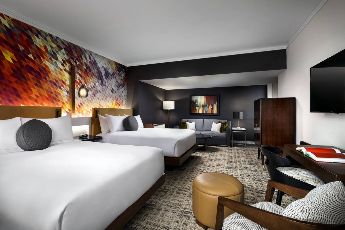 A hotel room with two beds, a sofa, a desk, and a TV.