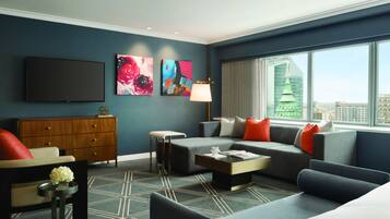 A modern hotel room with a large window, a flat-screen TV, a sofa, a coffee table, and artwork on the walls.