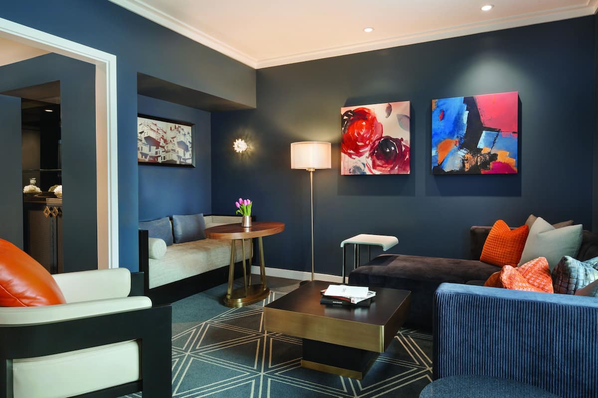 A modern living room with a sofa, armchair, coffee table, and artwork on the walls.