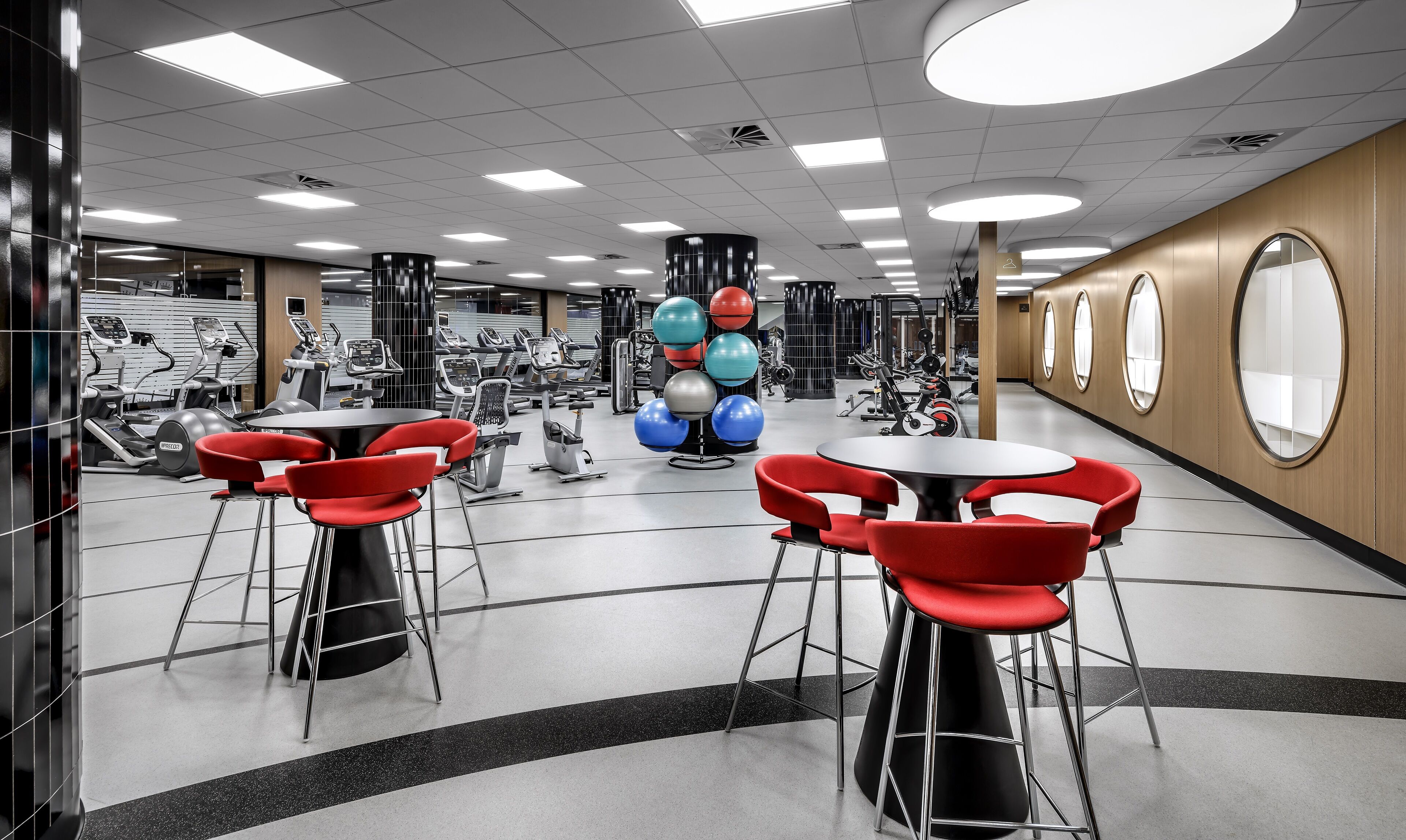 Un gimnasio con equipamiento de ejercicio, sillas rojas y un espejo grande.