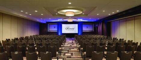 Un salón de conferencias con filas de sillas orientadas hacia un escenario con una pantalla que muestra “Fairmont Le Haut Elizabeth”.
