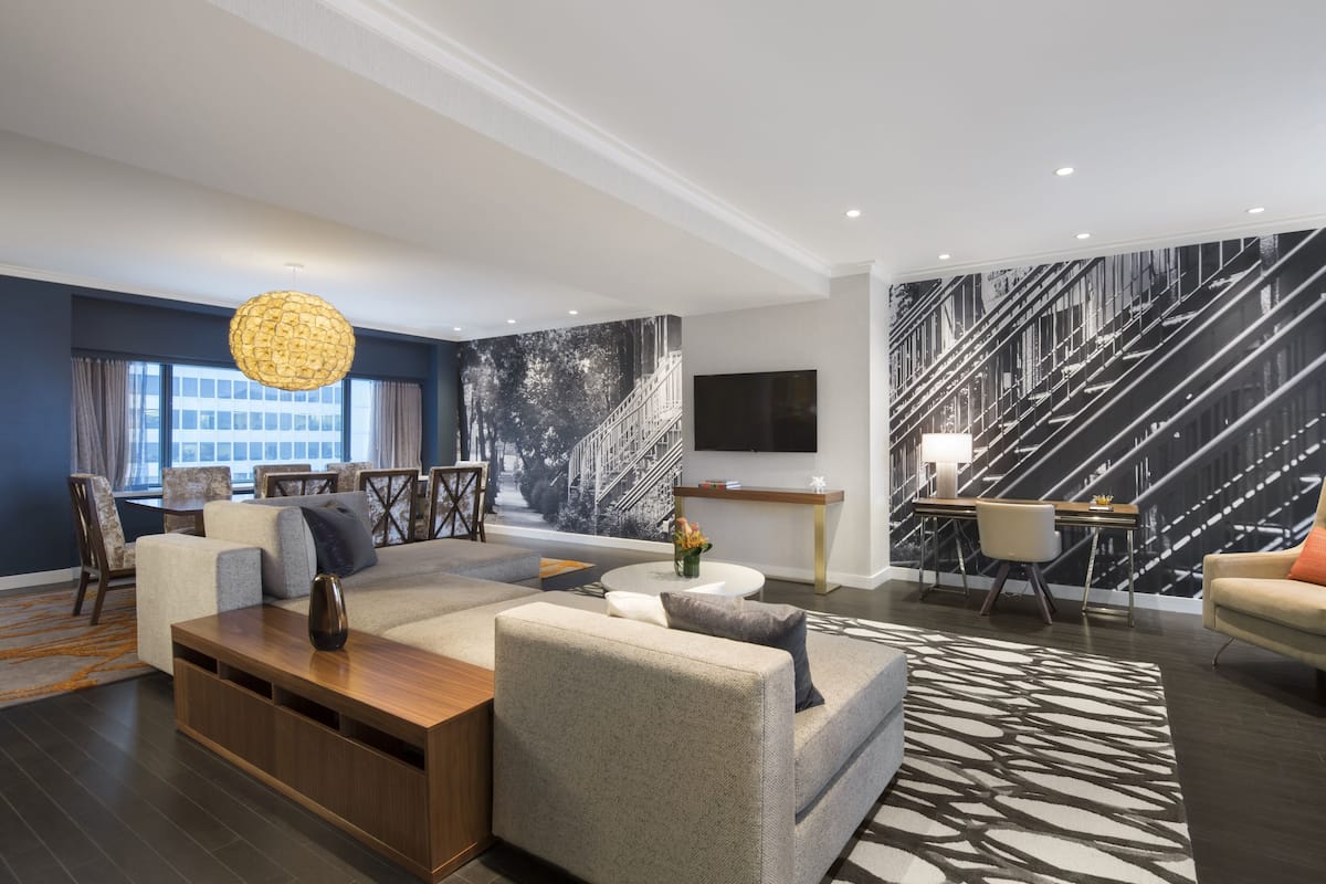 A modern living room with a sectional sofa, a coffee table, a TV mounted on the wall, and a staircase with a railing.