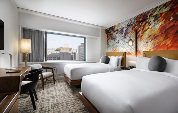 A hotel room with two beds, a desk with a chair, a lamp, and a view of the city through a large window. - Fairmont The Queen Elizabeth (Montreal)