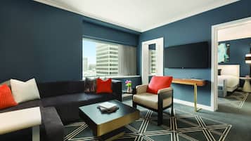 A modern living room with a black sofa, a beige armchair, and a coffee table. There is a large window with a view of a building.