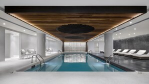 A modern indoor swimming pool with a sleek design, featuring a central water feature, lounge chairs, and a patterned ceiling. - Fairmont The Queen Elizabeth (Montreal)