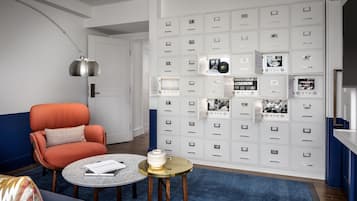 A modern living room with a blue sofa, an orange armchair, a round coffee table, and a wall of storage cabinets with photos and documents.