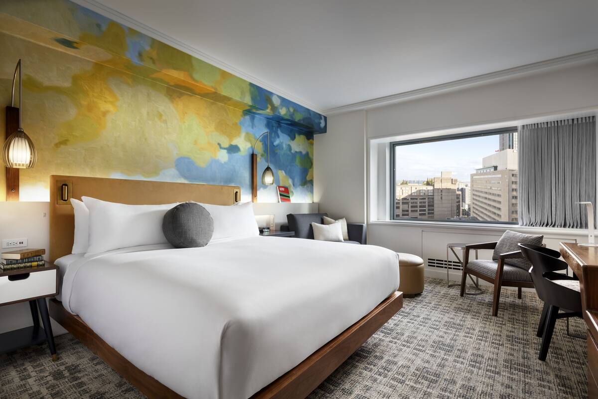 A modern hotel room with a large bed, a desk, and a view of the city.