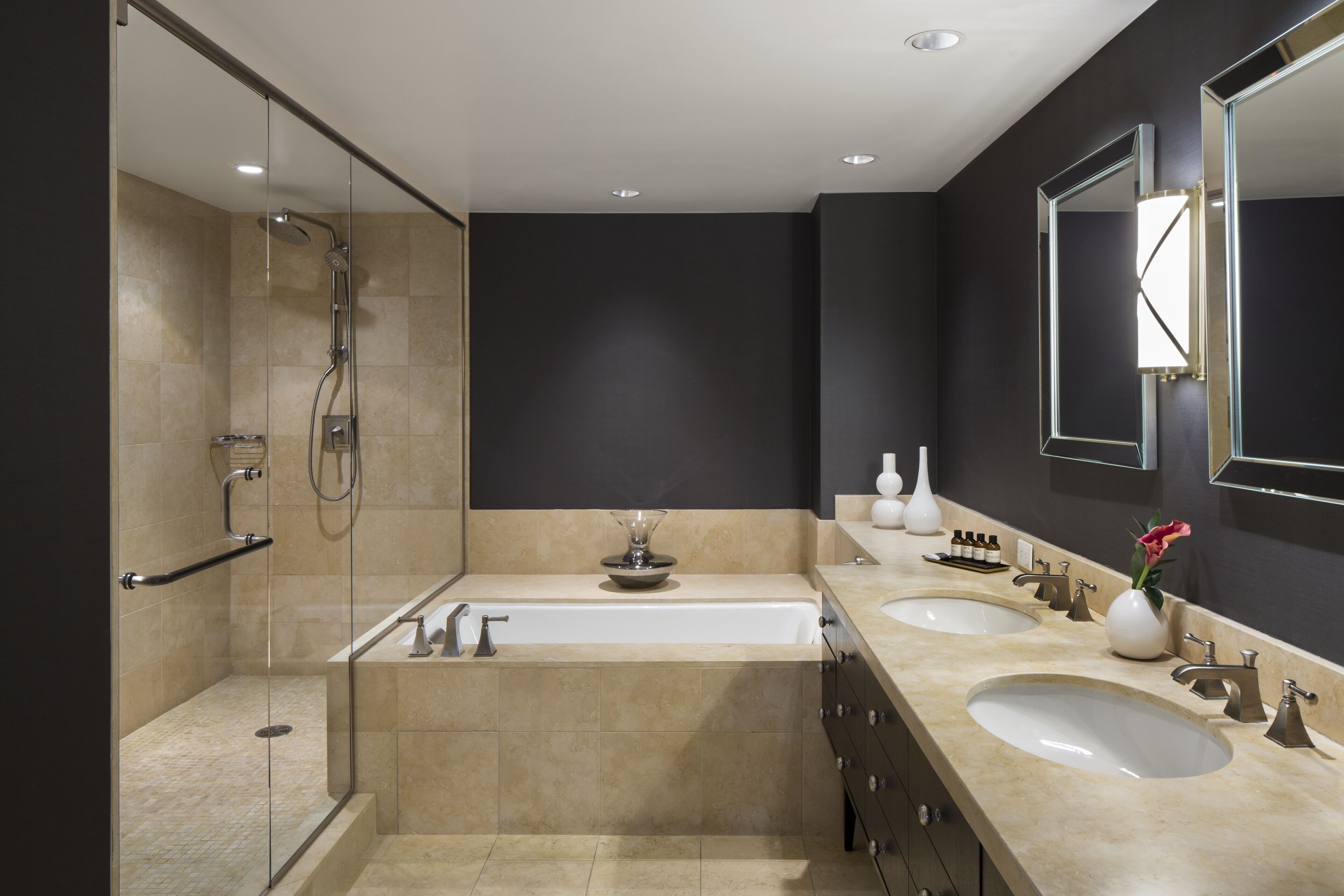 A modern bathroom with a glass-enclosed shower, a large bathtub, and two sinks.