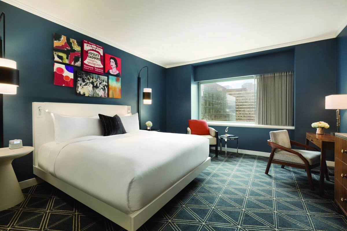 A hotel room with a large bed, a desk, a chair, and artwork on the walls.