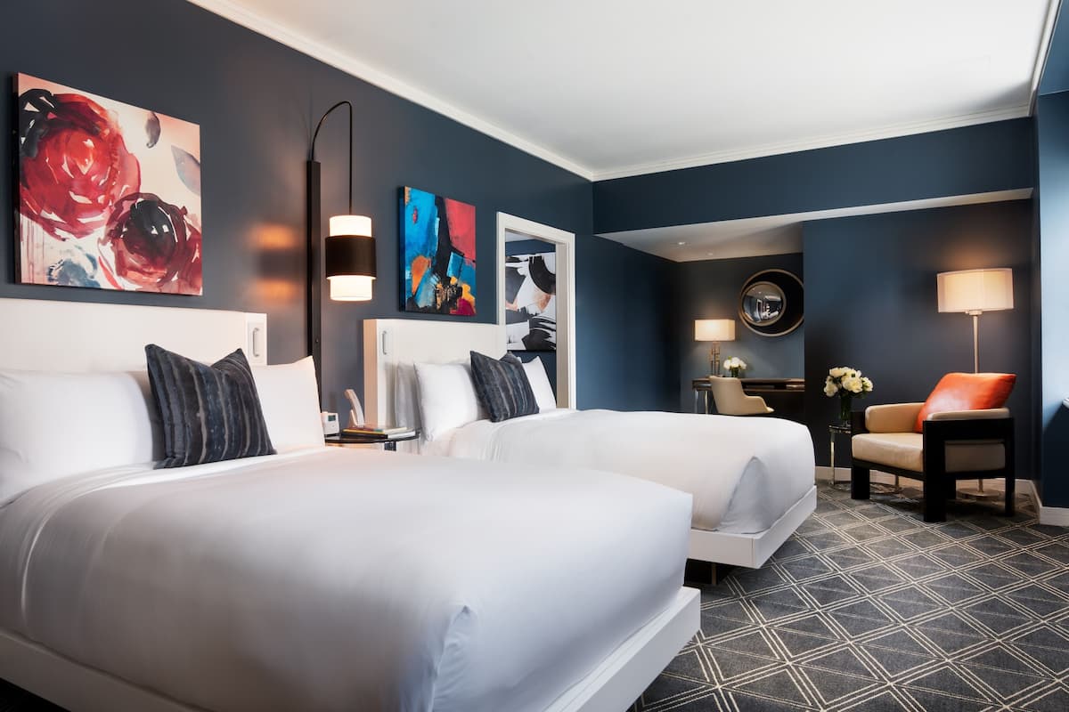 A hotel room with two beds, a desk, a chair, and artwork on the walls.
