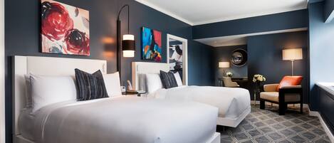 Une chambre d’hôtel avec deux lits, un bureau, une chaise et des œuvres d’art accrochées aux murs.