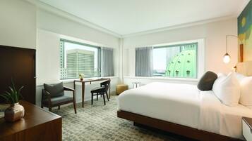 Une chambre d’hôtel avec un grand lit, un bureau avec une chaise, une petite table et une plante en pot.