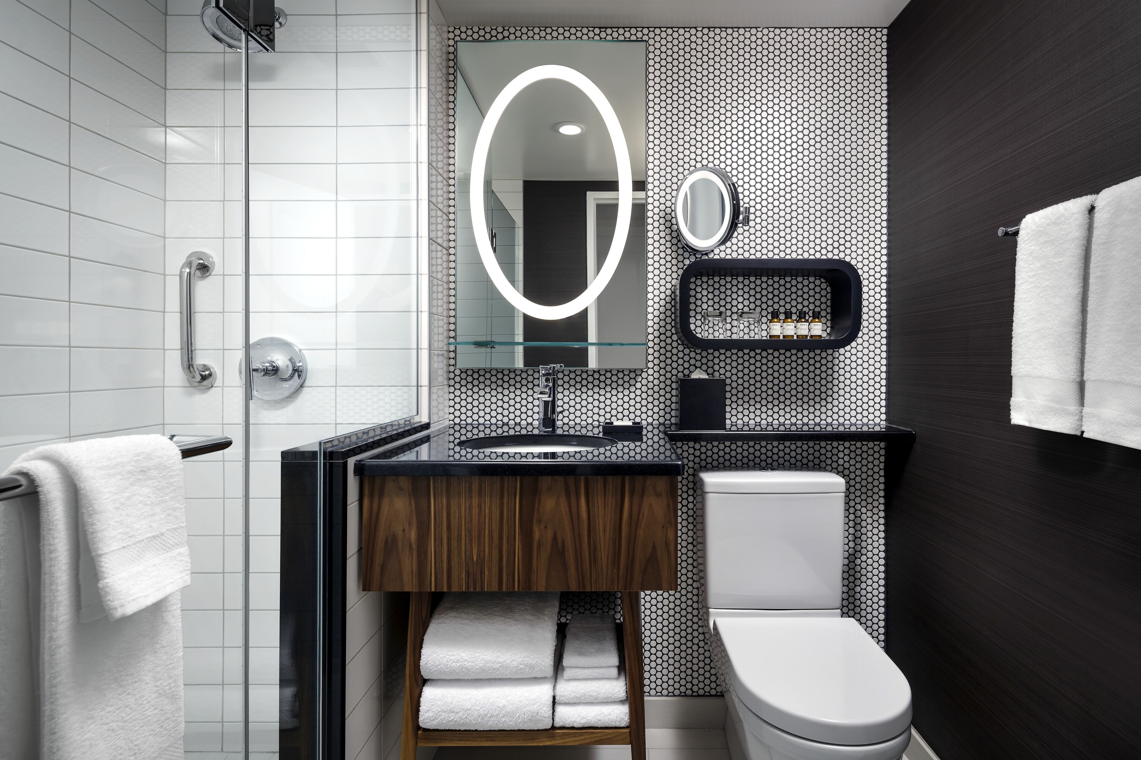 Une salle de bain moderne avec une douche à parois de verre, un meuble-lavabo en bois, des toilettes blanches et un mur orné d’un motif noir et blanc.