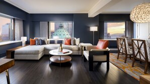 A modern living room with a sectional sofa, a round coffee table, and a dining area with chairs and a table. - Fairmont The Queen Elizabeth (Montreal)