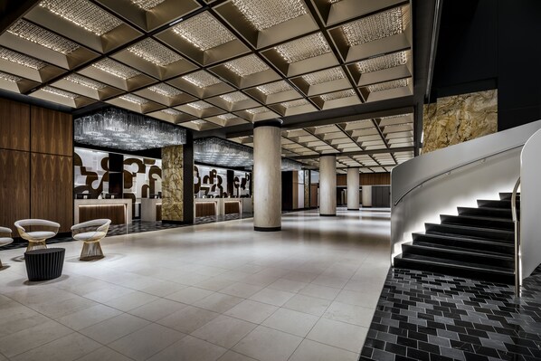 Un vestíbulo amplio con un diseño moderno, que incluye una recepción central, una escalera y una lámpara araña decorativa.