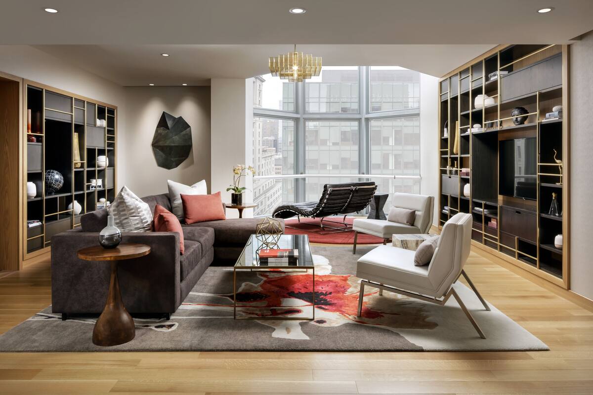 A modern living room with a large window, a sofa, a coffee table, and a bookshelf.