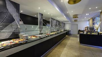 Montaje de bufé con diferentes opciones de comida, una barrera de vidrio e iluminación moderna.