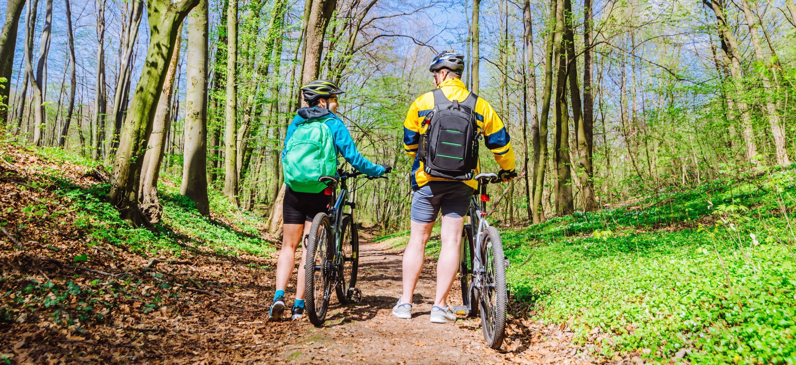 Dos ciclistas en un sendero forestal, rodeados de árboles y follaje.